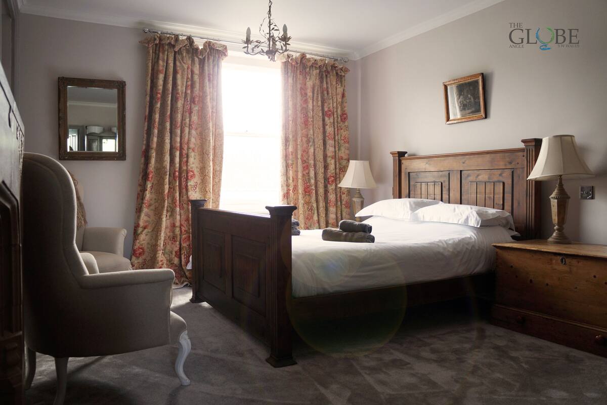 A bedroom with a wooden bed, a chair, a dresser, a mirror, and a window with floral curtains.