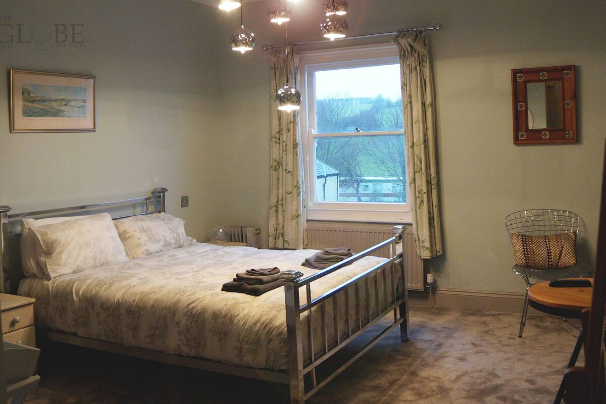 A bedroom with a bed, bedside table, window, and a chair.
