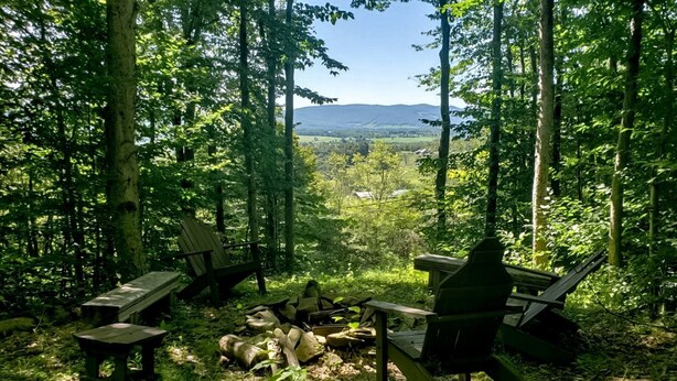 Ein Waldcampingplatz mit Adirondack-Stühlen, einer Feuerstelle und Blick auf ferne Berge.