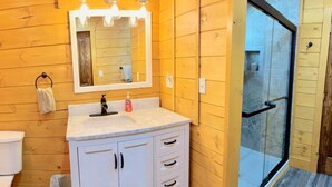 Une salle de bain avec un mur en bois, un lavabo avec un miroir et une porte de douche en verre.