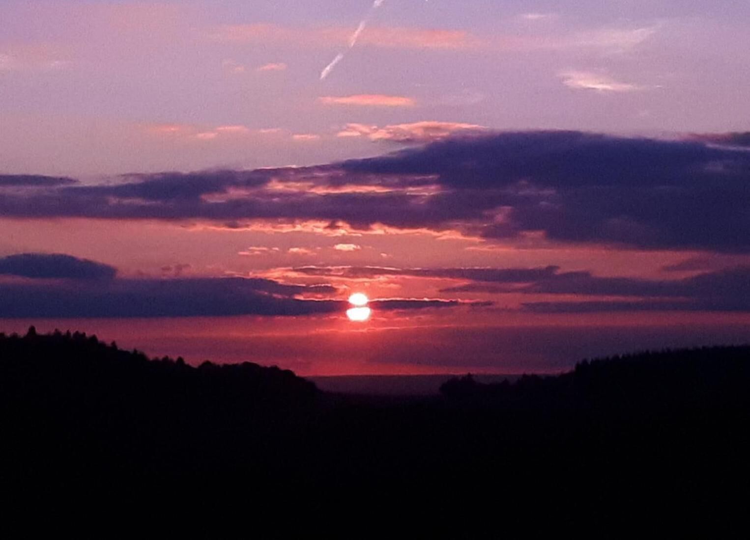 Tramonto su un paesaggio boschivo con linea dell'orizzonte ben visibile.
