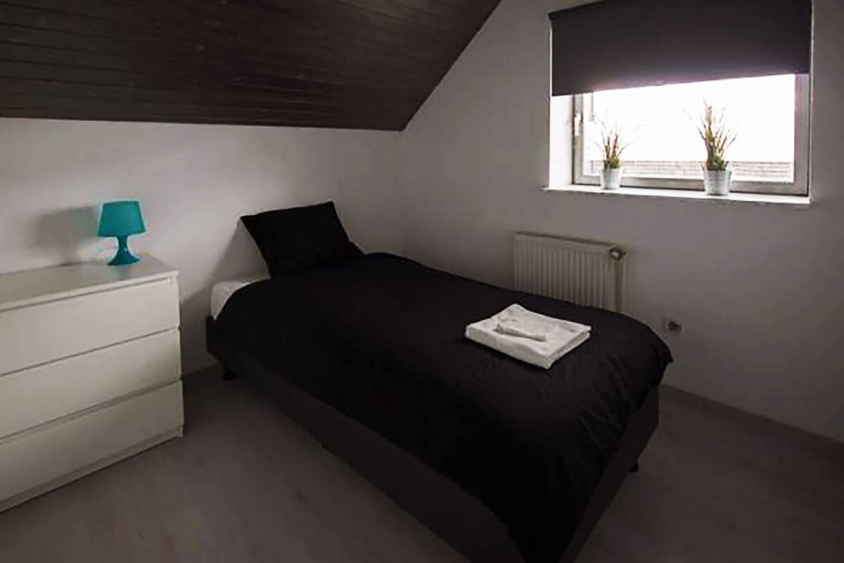 Un dormitorio con cama, mesita de noche, ventana con plantas y radiador.
