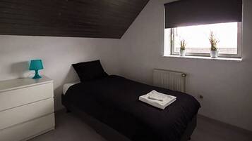 A bedroom with a bed, a nightstand, a window with plants, and a radiator.