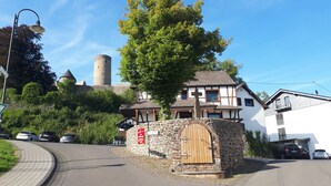A traditional building with a stone entrance, a sign indicating a restaurant, and a view of a castle in the background. -  DF am Ring Nürburg (Nuerburg)