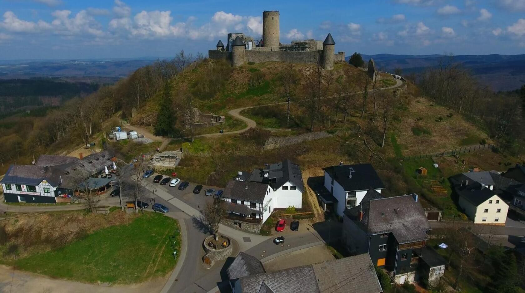 Un castillo en una colina con un pueblo abajo, que incluye casas y una carretera.