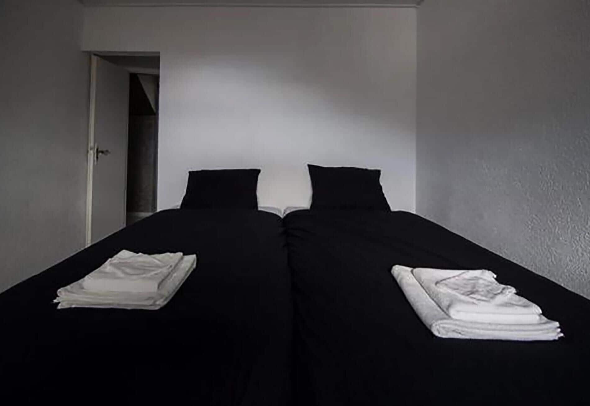 A room with two single beds, each with a folded white towel.