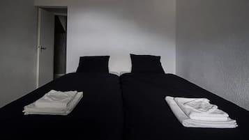 A room with two single beds, each with a folded white towel.