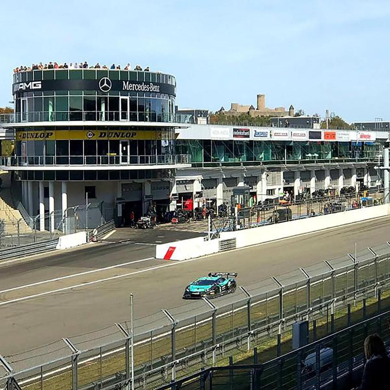 A race track with a Mercedes-Benz building and a blue car on the track.