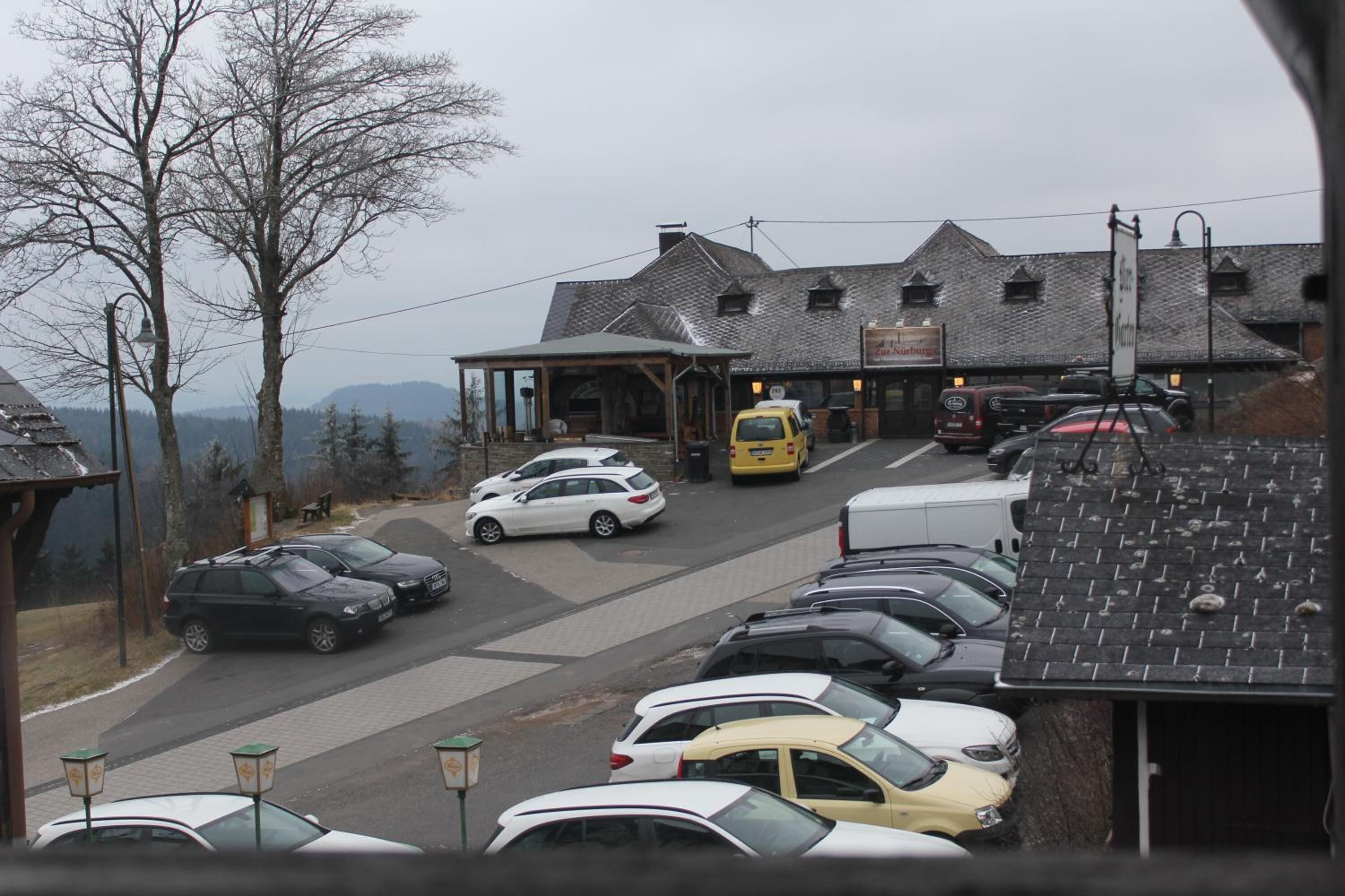 A parking lot with several cars parked in front of a building with a sloped roof and a signboard.