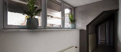 A hallway with a radiator, a window with two potted plants, and a staircase leading to another floor.