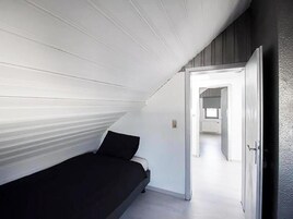 A room with a sloped ceiling, a bed, and a door leading to another room.