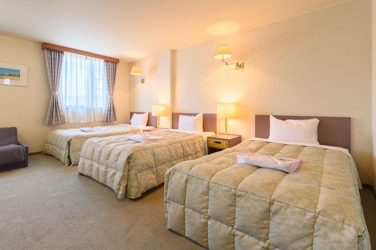 A hotel room with two beds, a chair, and a nightstand with lamps.