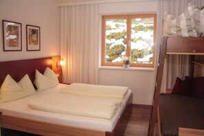 A bedroom with a wooden bed, a window with a view of snow-covered trees, and two framed pictures on the wall. - Cozy apartment with sauna (Saalbach)