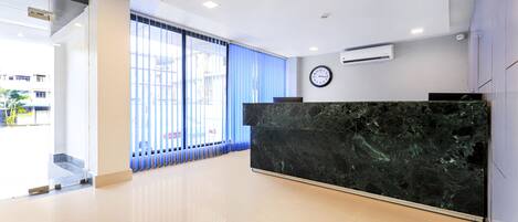 A modern reception area with a marble counter, a clock, and a large window with blinds.