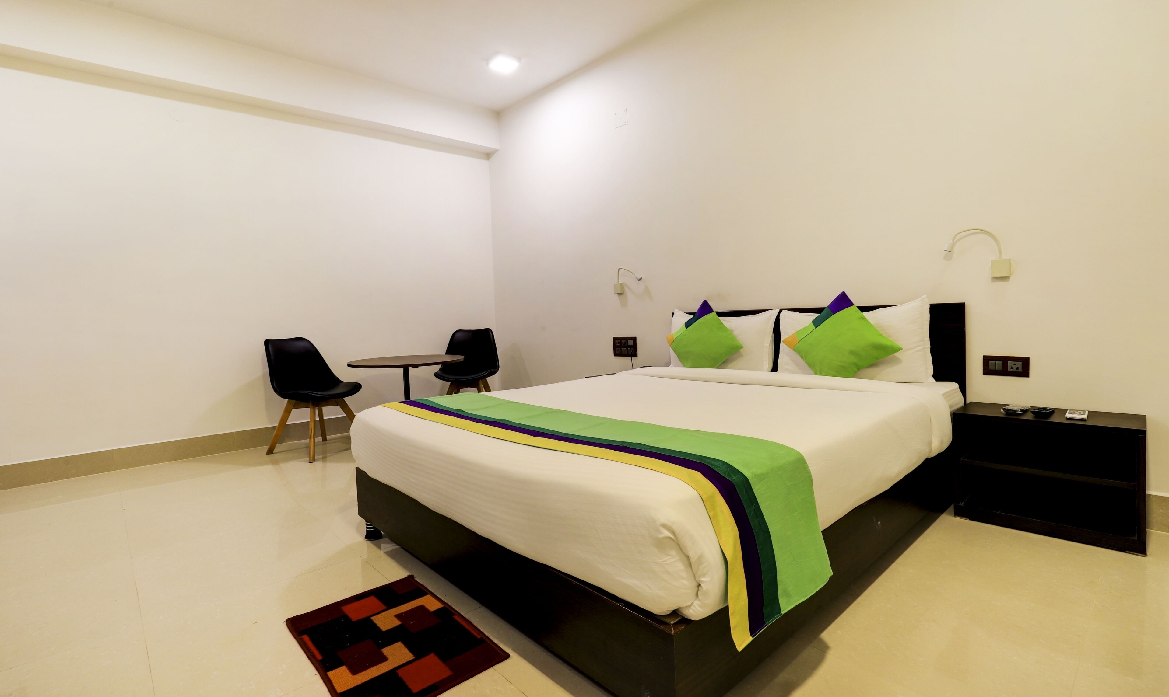 Moderni hotellihuone, jossa on suuri sänky, työpöytä, kaksi tuolia ja pieni pöytä.