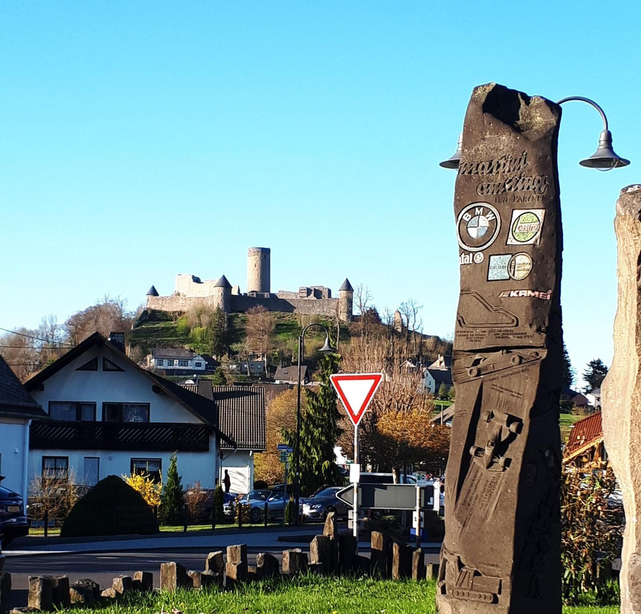 Een middeleeuws kasteel op een heuvel, met een moderne sculptuur op de voorgrond.