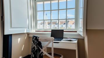 Una habitación con escritorio y silla cerca de una ventana, una computadora portátil sobre el escritorio y un abrigo colgado en la silla.