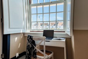 Una habitación con escritorio y silla cerca de una ventana, una computadora portátil sobre el escritorio y un abrigo colgado en la silla.