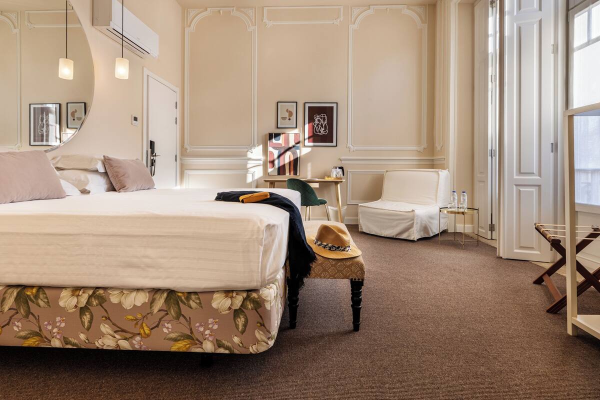 A hotel room with a large bed, a small table, a chair, and a window.