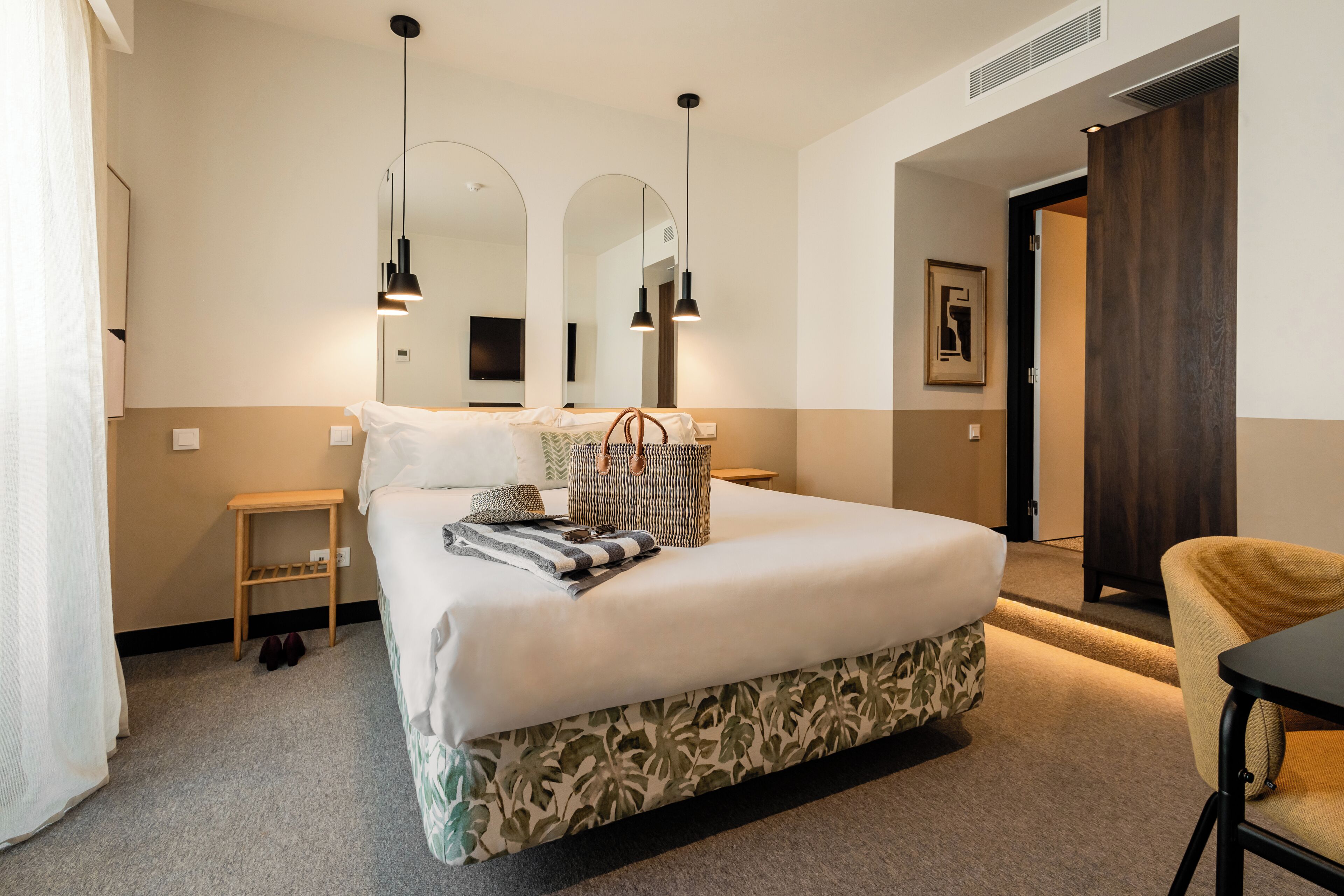 A neatly arranged hotel room with a large bed, bedside tables, a chair, and a mirror.