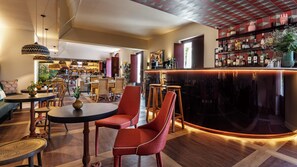 Zona de bar moderna con una barra curva y una variedad de botellas. Se observan sillas de mimbre y una mesa redonda en primer plano.