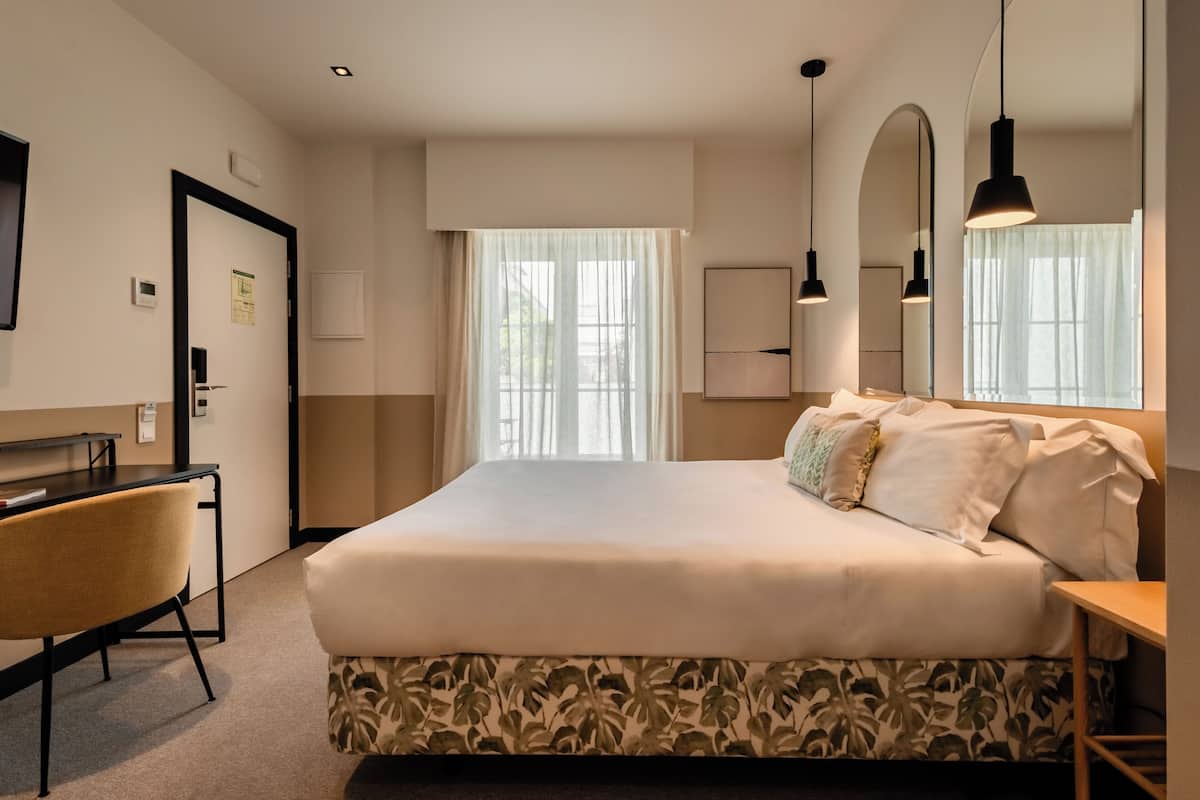 A hotel room with a bed, a desk, a chair, and a large window with curtains.