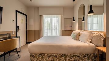 A hotel room with a bed, a desk, a chair, and a large window with curtains.