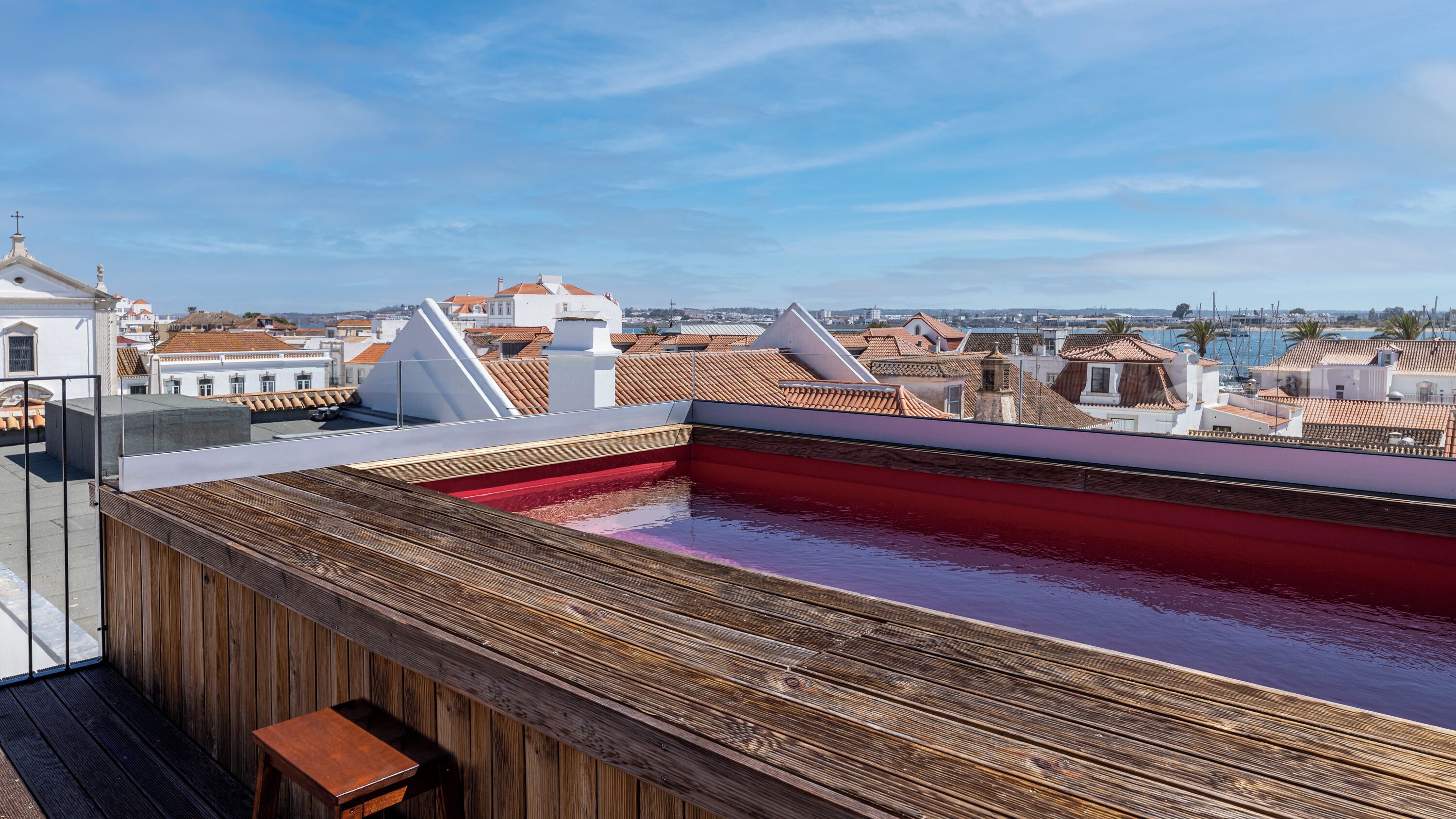 A rooftop swimming pool with a wooden deck and a view of the cityscape.