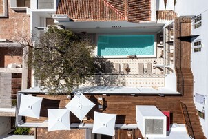 Una piscina en la azotea con vistas a la ciudad, rodeada de edificios modernos y un árbol.