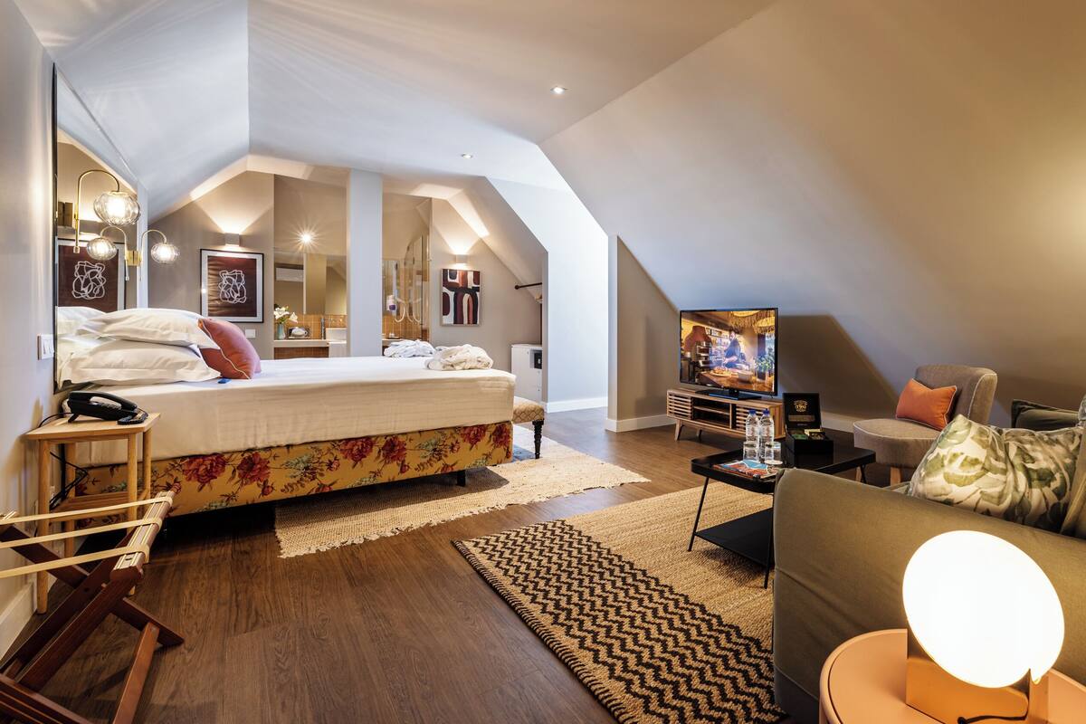 A modern, well-lit bedroom with a large bed, a TV, and a cozy seating area.