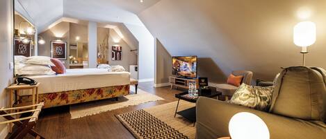 A modern, well-lit bedroom with a large bed, a TV, and a cozy seating area.