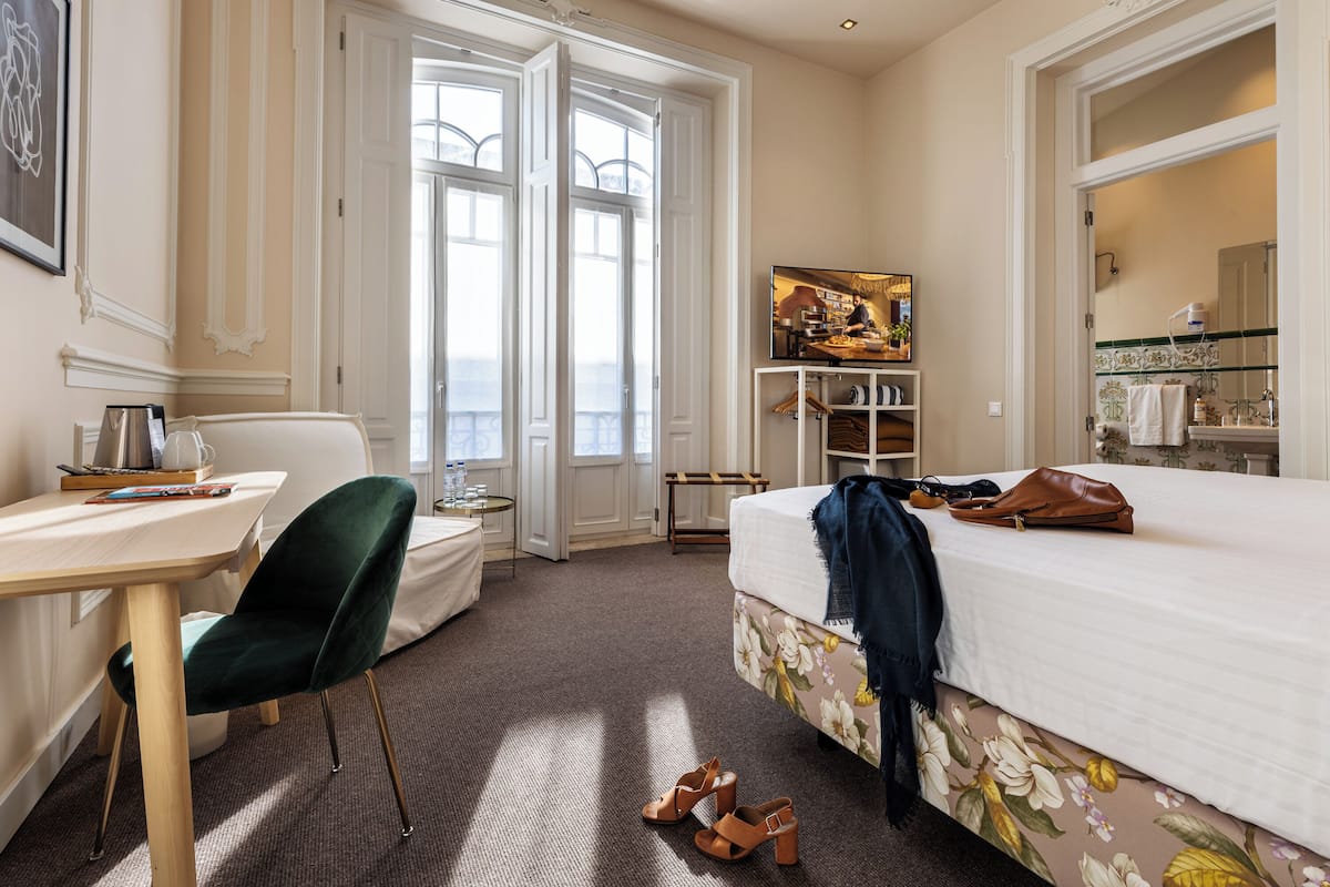 A hotel room with a bed, a desk, a chair, a wardrobe, and a large window.