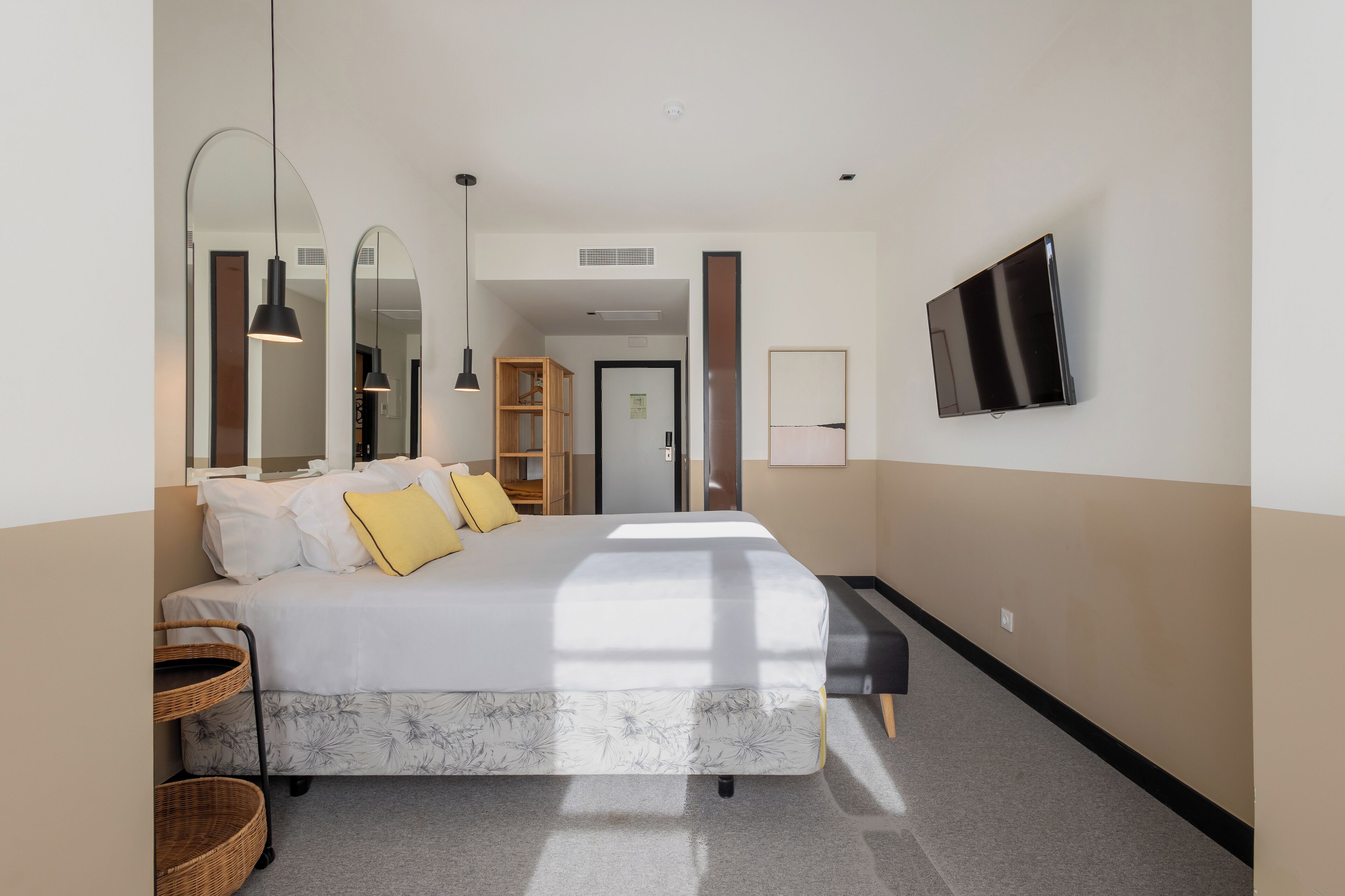 Ein modernes Hotelzimmer mit einem großen Bett, einem Flachbildfernseher, einem Spiegel und einem Holzschrank.