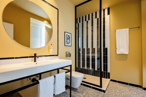 Un baño moderno con un espejo grande, un lavabo blanco, un inodoro y una ducha con azulejos blancos y negros.
