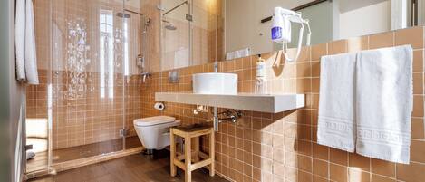 Un baño moderno con ducha de vidrio, un taburete de madera, un lavamanos blanco y un perchero para toallas.