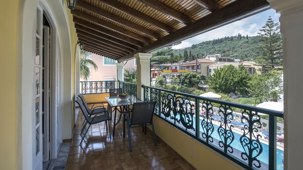 A balcony with a view of a swimming pool, a table with chairs, and a wooden ceiling. - Andreas Pool Complex (Corfu)