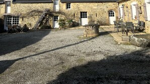 Un bâtiment en pierre doté de nombreuses fenêtres et portes, une cour recouverte de gravier et un ciel d’un bleu limpide.