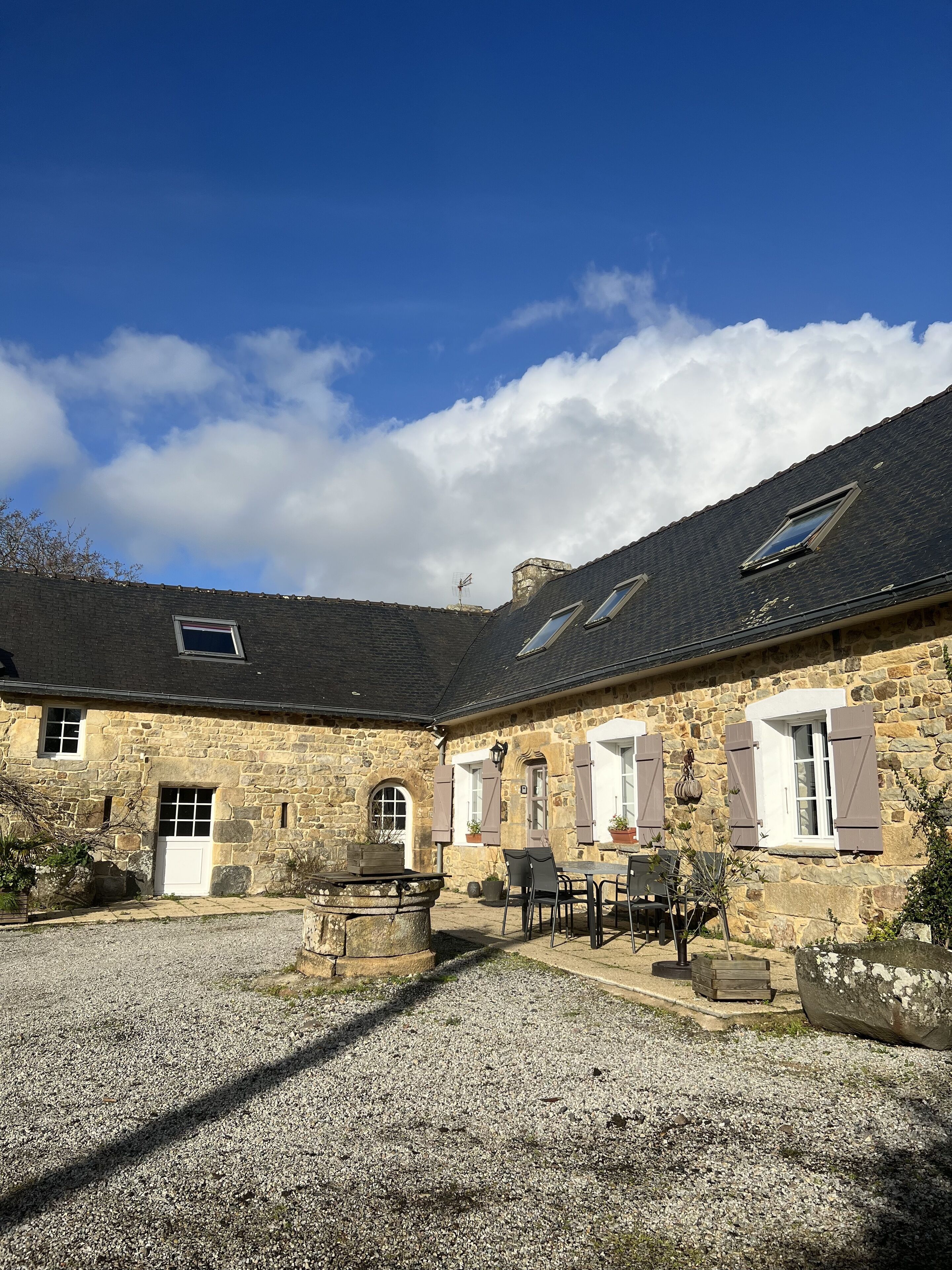 A stone building with a gravel courtyard, multiple windows, and a sloped roof.
