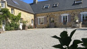 Un bâtiment en pierre avec une cour recouverte de gravier, des fenêtres avec des volets et une porte.