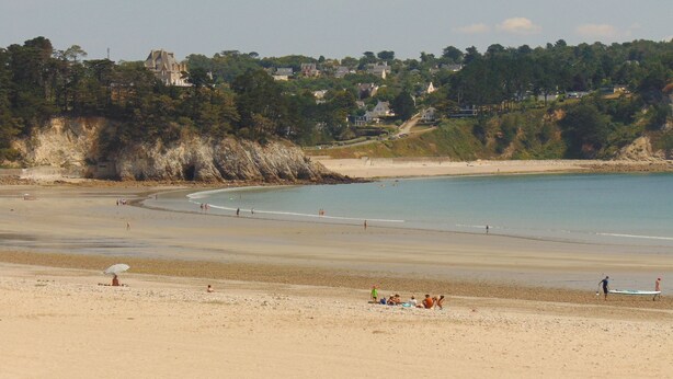 Une plage avec un rivage sablonneux, quelques personnes et un bâtiment en arrière-plan.