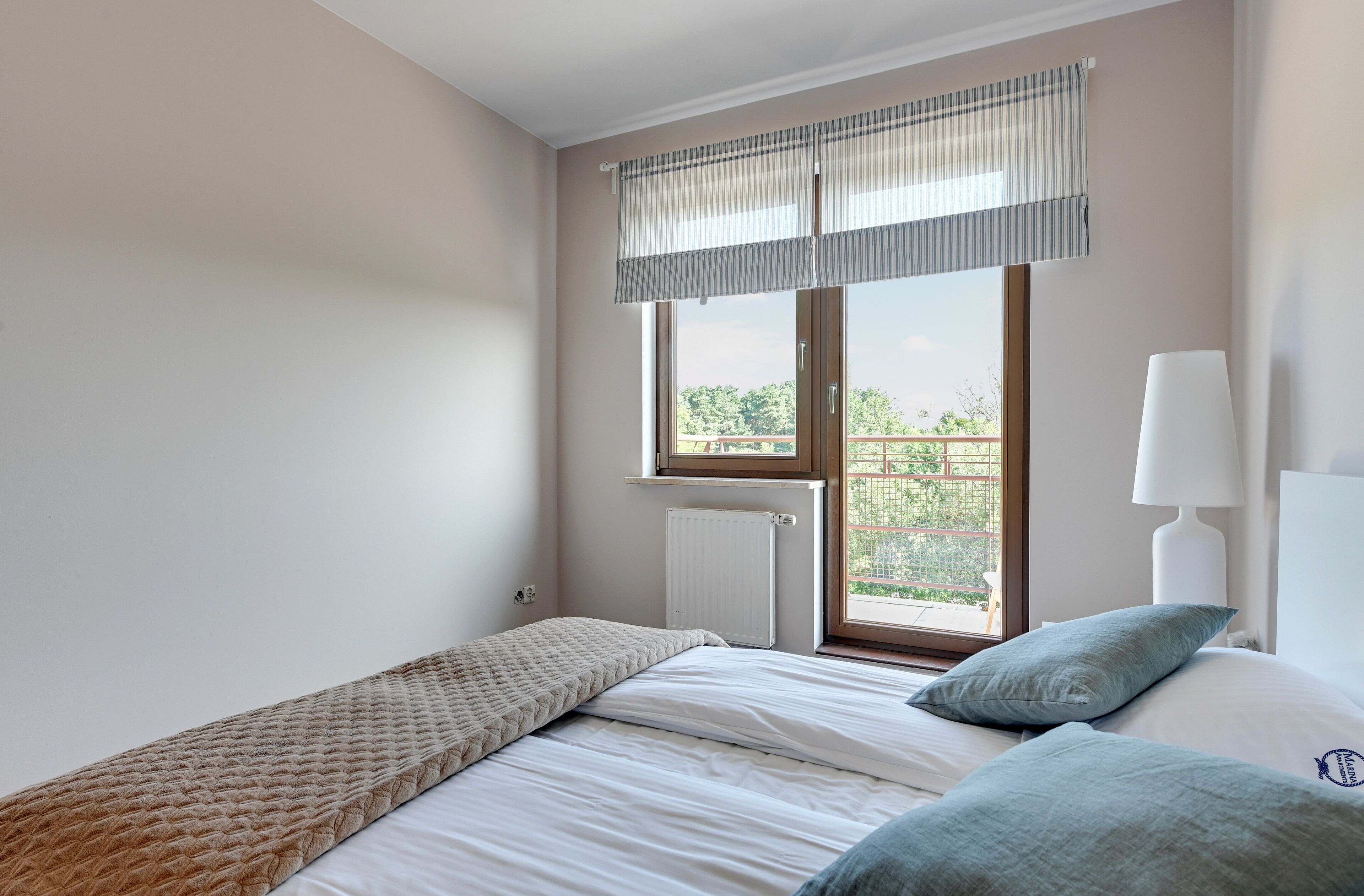 A bedroom with a bed, a window with a view, a radiator, and a lamp.