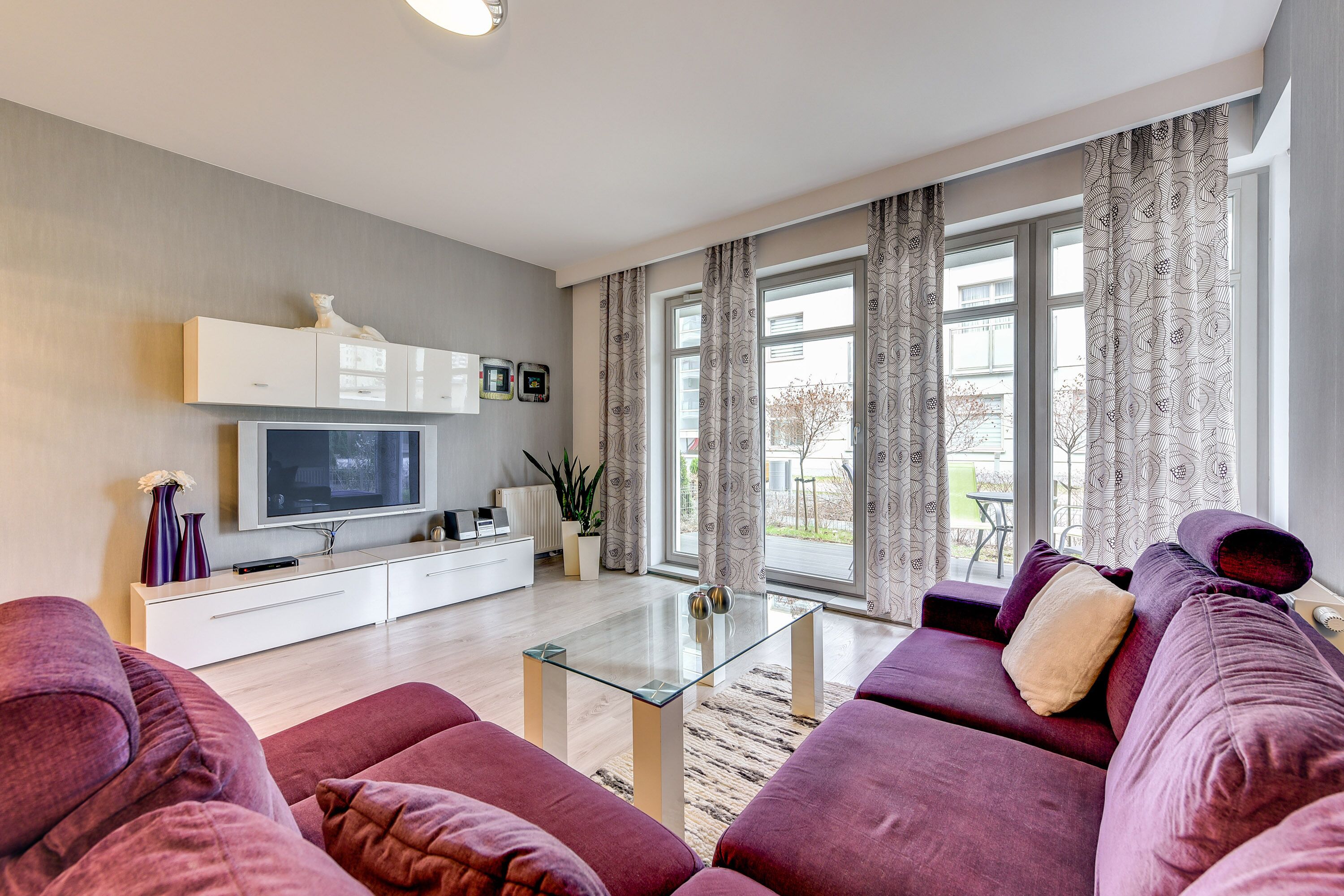 Ein modernes Wohnzimmer mit einer Sofagarnitur, einem Glastisch, einem Flachbildfernseher und einer weißen Kommode.