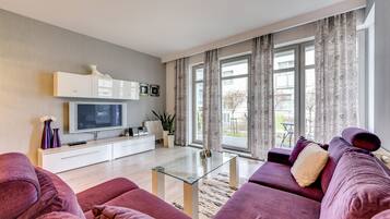 Ein modernes Wohnzimmer mit einer Sofagarnitur, einem Glastisch, einem Flachbildfernseher und einer weißen Kommode.