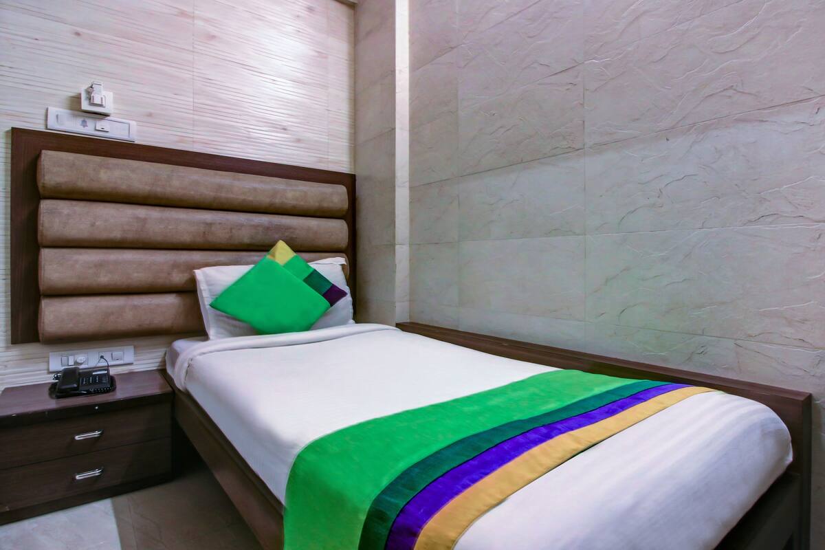 A hotel room with a bed, a nightstand, a telephone, and a wall socket.