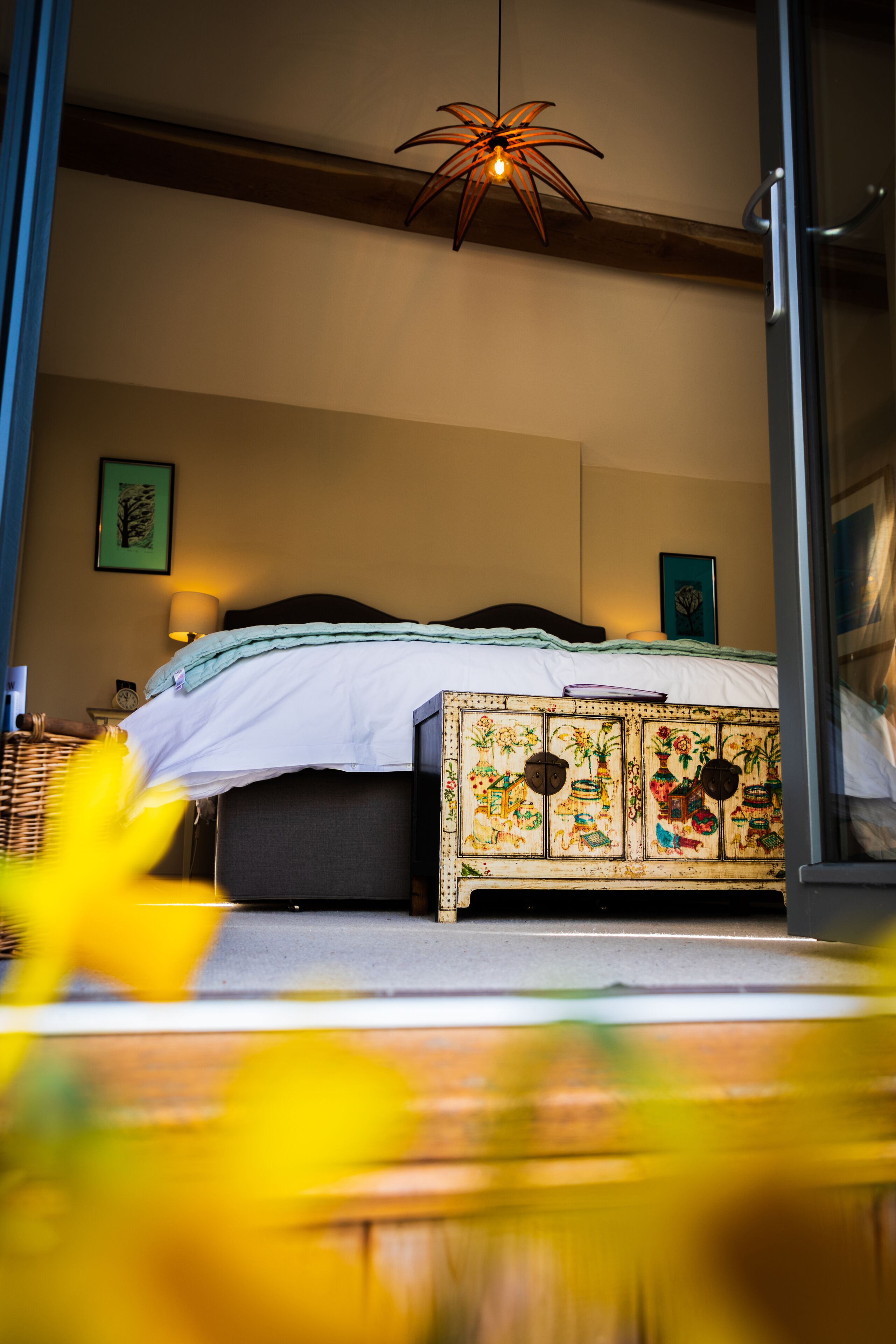 A bedroom with a bed, a decorative cabinet, a hanging light fixture, and a framed picture on the wall.