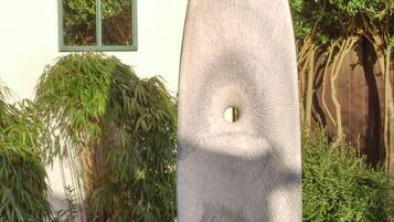 Un jardín con una gran escultura blanca, una ventana y diversas plantas.