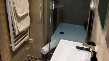 Un baño con ducha compartimentada con vidrio, un lavamanos blanco y un perchero con toallas dobladas.