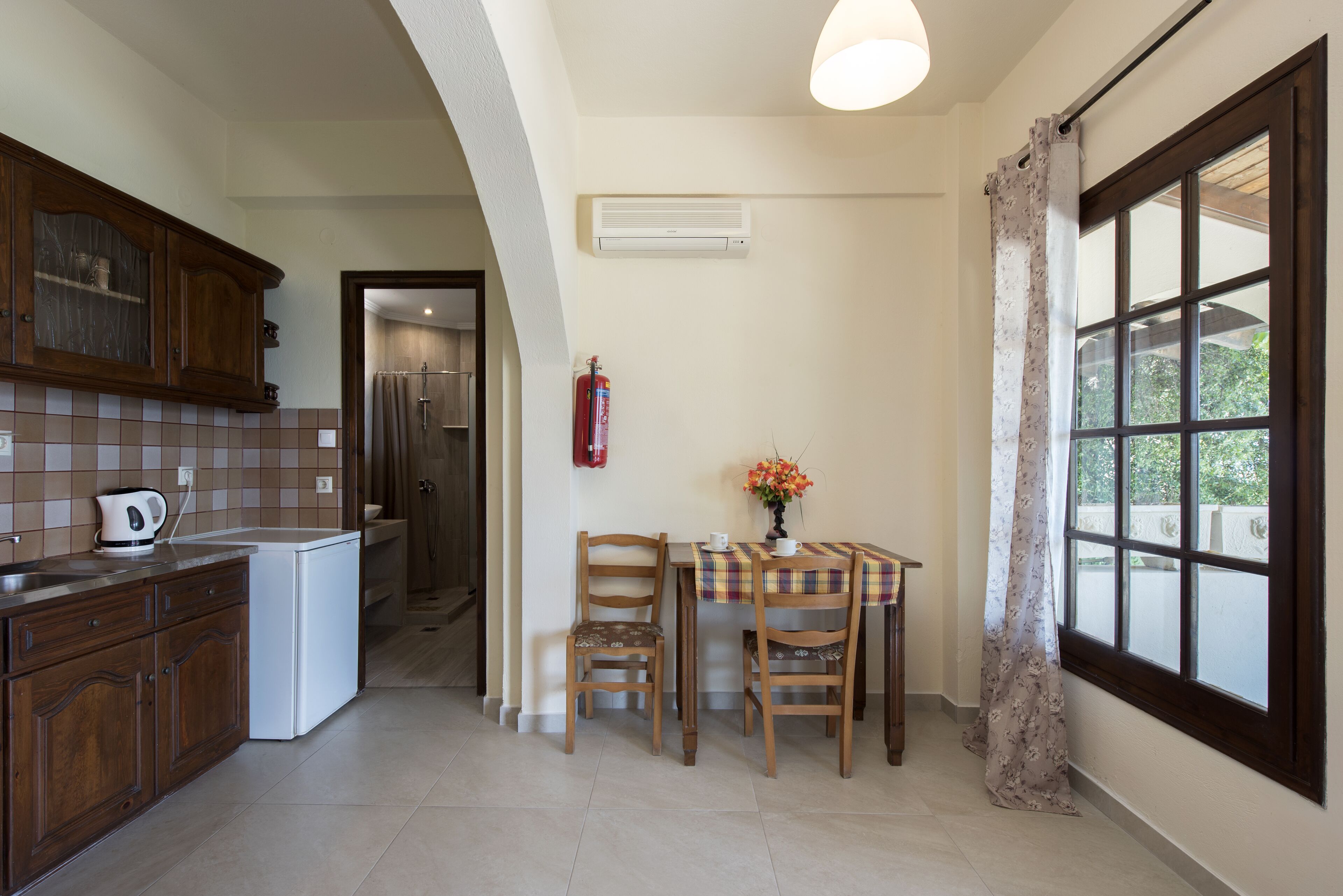 A kitchen with wooden cabinets, a white refrigerator, a dining table with chairs, and a window with curtains.