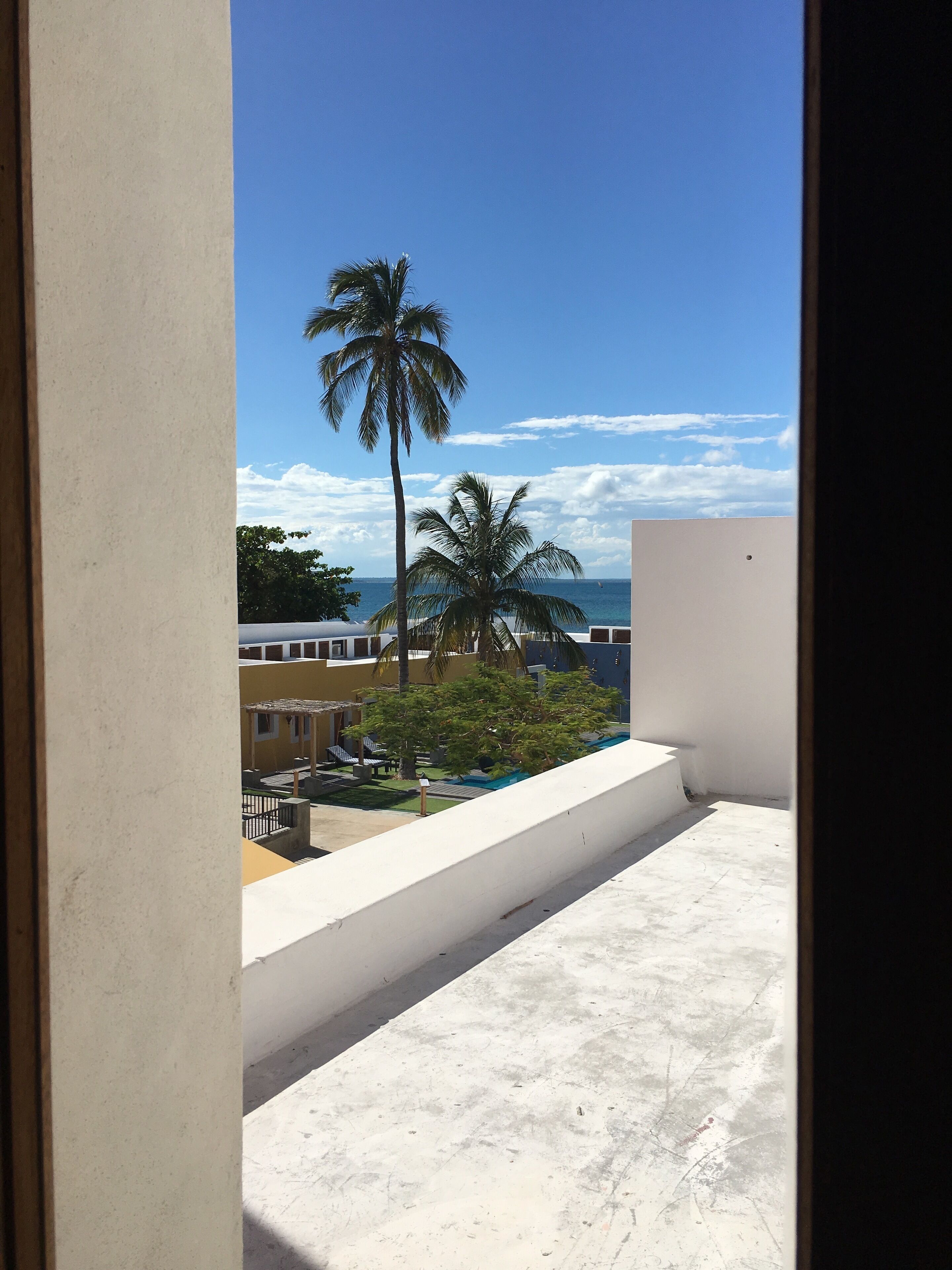 A balcony with a view of the sea, palm trees, and buildings.