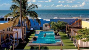 A pool area with a view of the ocean, surrounded by palm trees and a building with a blue facade. - Feitoria Boutique Hotel (Mozambique Island)